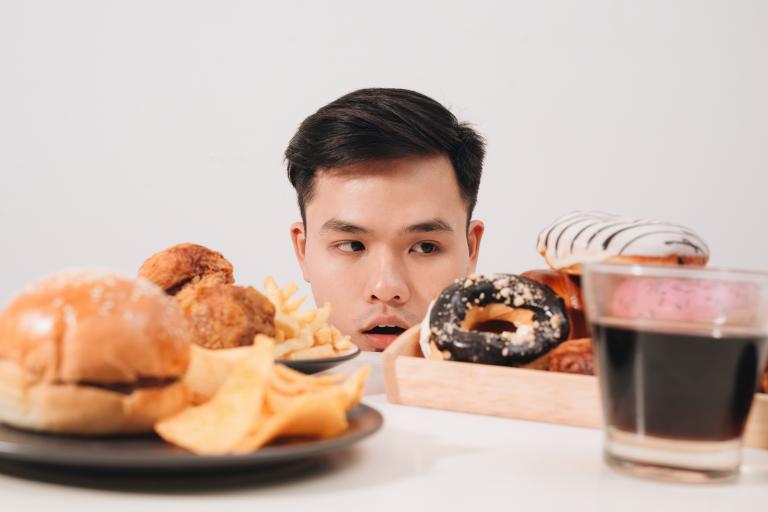 Young man having cravings for donuts, hamburger, chicken with fries.