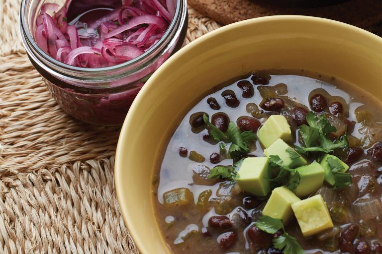 A bowl of black bean soup garnished with lime-pickled red onion and avocado